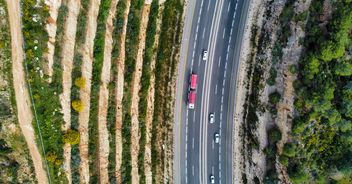 Drone shot capturing a highway with vehicles, surrounded by terraced landscape.