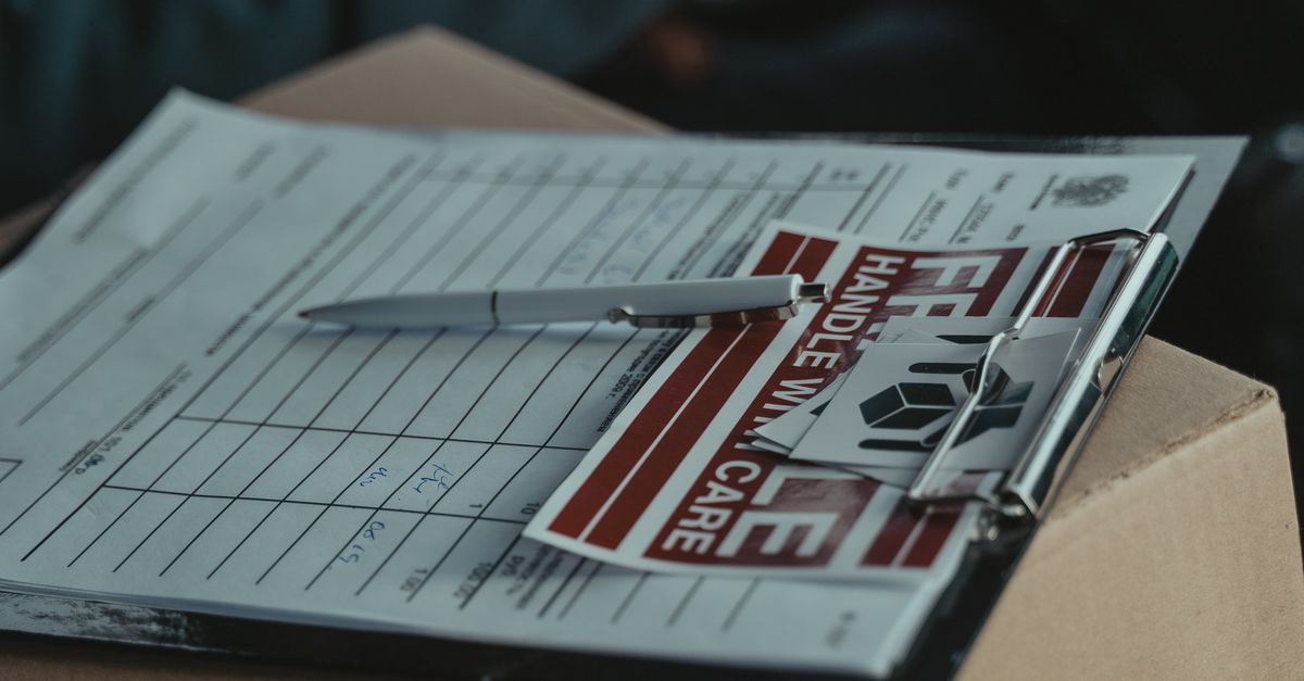 A clipboard with delivery papers and a 'Handle with Care' sticker on a cardboard box.
